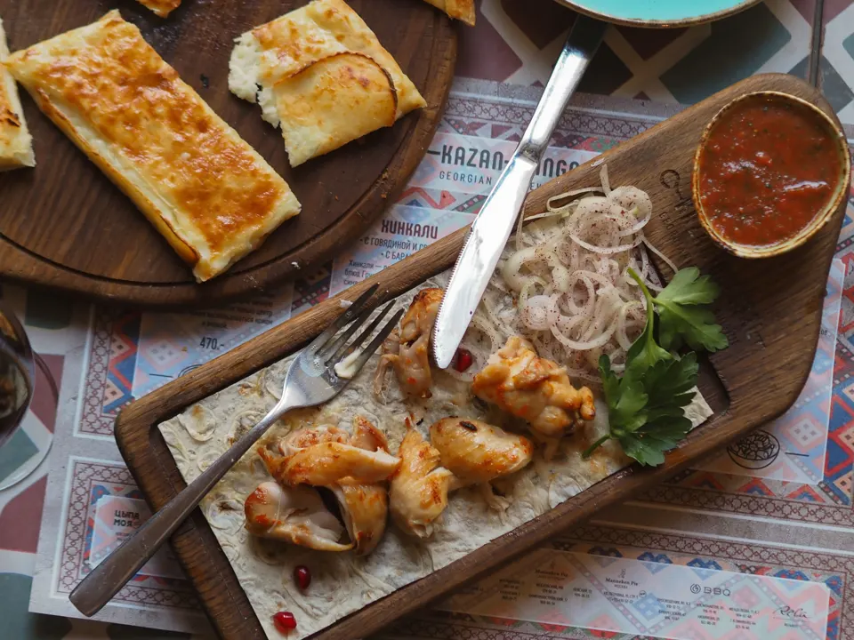 Georgian restaurant table with khachapuri, grilled meat, onions, herbs, and red sauce