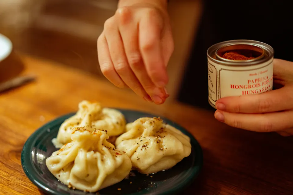 Person seasoning khinkali Georgian dumplings at a restaurant table